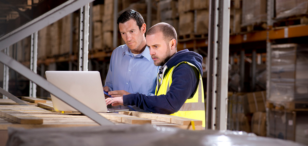 Two people in a warehouse looking at a laptop computer