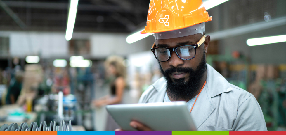 A man with a yellow hardhat on looking at a tablet in a warehouse