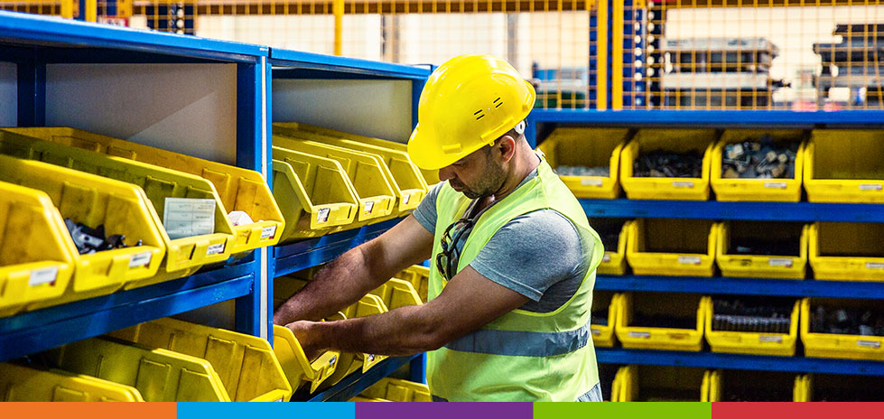 Hombre con un casco amarillo sacando sujetadores de un contenedor amarillo administrando su inventario